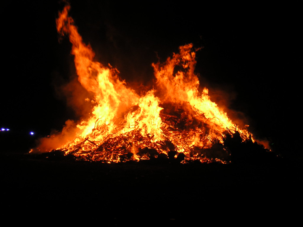 Image of a bonfire burning brightly. The background is pitch black as it is night time.
