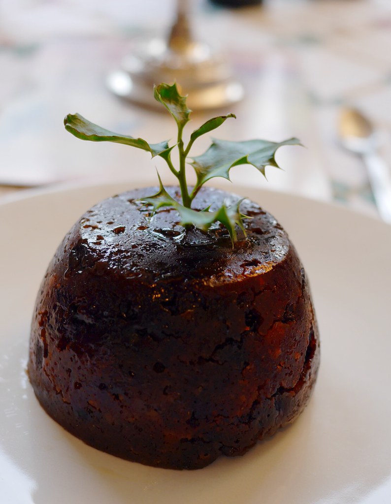 A small brown Christmas pudding with a sprig of holly leaf sticking out of the top.