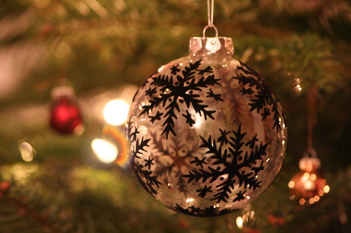 A close up of a silver bauble with black snowflakes hanging on a Christmas tree.